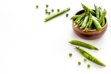 Green pea pods in wooden bowl on the kitchen background