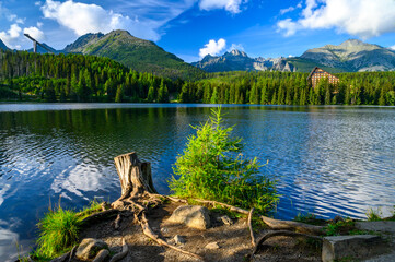 Mountain lake Strbske pleso in the Tatra National Park. In the background rocky peaks, pine forests and blue sky with clouds.
