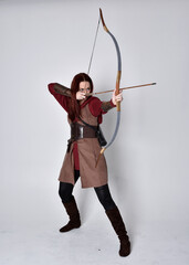 Full length portrait of girl with red hair wearing  brown medieval archer costume.. Standing pose...