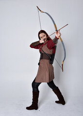 Full length portrait of girl with red hair wearing  brown medieval archer costume.. Standing pose...