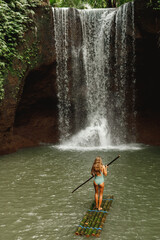 Fototapeta na wymiar Travel wwoman alone at the tropical wild nature adventure on the bamboo raft in front of the waterfall in jungle