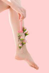 Woman's thin unshaven leg with pink flowers on a pink background. Female shaves her leg with a pink razor. Feminism