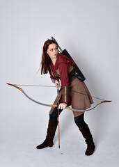 Full length portrait of girl with red hair wearing  brown medieval archer costume.. Standing pose...