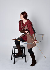 Full length portrait of girl with red hair wearing  brown medieval archer costume.. Standing pose...