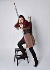 Full length portrait of girl with red hair wearing  brown medieval archer costume.. Standing pose...