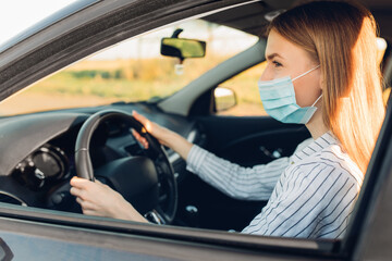 Fototapeta na wymiar Beautiful young woman in a protective medical mask on her face, driving a car during a trip, travel concept