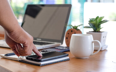 Fototapeta premium a young man working from home using a smartphone and laptop computer man. Side view shot of hands using a smartphone, the man at his workplace.
