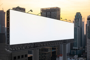 Obraz premium Blank white road billboard with Bangkok cityscape background at sunset. Street advertising poster, mock up, 3D rendering. Side view. The concept of marketing communication to promote or sell idea.