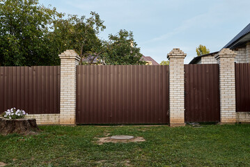 Metal brown fence, gate and wicket made of corrugated board and brick of a country house
