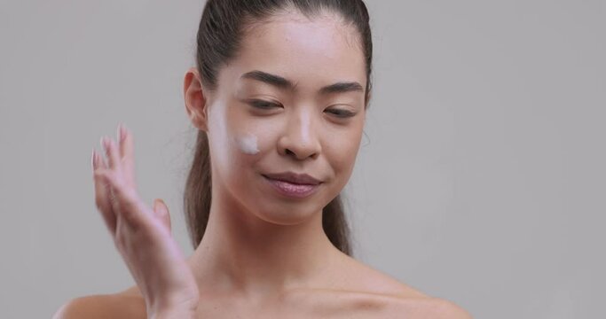 Portrait of young asian woman applying cream smear on cheek and smiling to camera