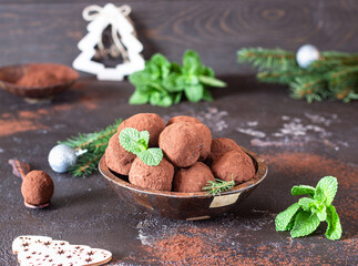 Dark chocolate truffles with raw cocoa powder, mint and fir tree branches, dark brown stone background. Christmas composition. 