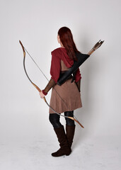 Full length portrait of girl with red hair wearing  brown medieval archer costume.. Standing pose...
