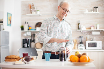 Senior man making coffee with use of a french press during breakfast in kitchen. Elderly person in the morning enjoying fresh brown cafe espresso cup caffeine from vintage mug, filter relax