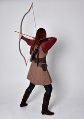 Full length portrait of girl with red hair wearing  brown medieval archer costume.. Standing pose...