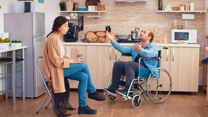 Handicapped man in wheelchair having a dispute with wife in kitchen. Guy with paralysis handicap...