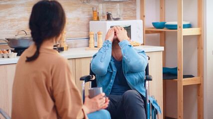 Disabled man in wheelchair having a conflict with wife in kitchen. Guy with paralysis handicap disability handicapped difficulties getting help for mobility from love and relationship