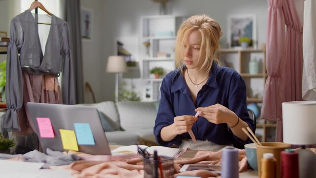 Beautiful young girl fashion designer communicates with the client via video call at home in the living room