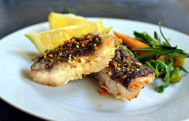 Grilled fish with lemon, herbs and rosemary. Fried fish fillets in a white plate. Beautiful presentation of food. Rucolla salad and carrots. Close-up.