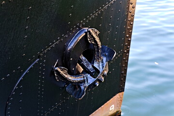 Black iron anchor secured on an old black steel tug with rivets.