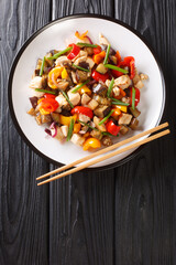 Asian stir fry chicken with eggplant, pepper and onion close-up in a plate on the table. vertical top view from above