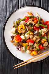 stir-fried chicken with eggplant, pepper and onion close-up in a plate on the table. Vertical top view from above