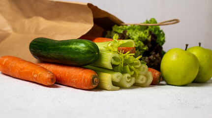 Vegetables in a paper bag on a white table: carrots, celery, cucumbers, zucchini, apples, cabbage, lettuce. The concept of grocery delivery