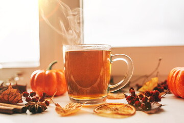 Hot steaming Cup of tea with autumn leaves, pumpkins and spices on the windowsill. Autumn mood.