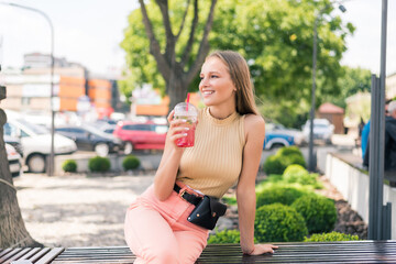 Young pretty woman walking on the street with take away drink in the transparent cup in the city