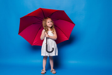 Happy funny child with red umbrella posing on blue wall background.