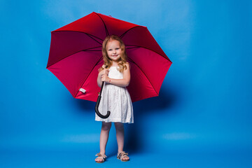 Happy funny child with red umbrella posing on blue wall background.