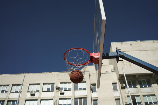 Image of basketball shot in hoop on city sports ground at summer day