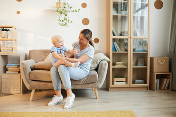 Young mother spending time at home sitting on sofa with her baby son in living room, copy space