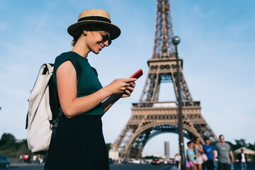 Fototapeta na wymiar Caucasian woman browsing wireless network during time for romantic French walk in Paris, carefree female tourist enjoying smartphone communication standing at street with Eiffel Tower on background