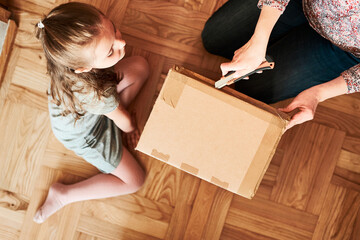 Woman unpacking a cardboard box parcel in room at home. Little girl waiting for opening a gift in...