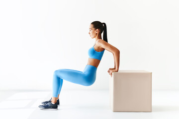 Sporty woman practicing squat exercises with big cube over white background.