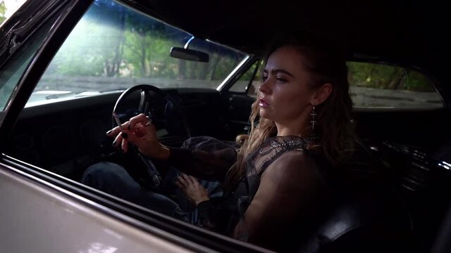 Close up of a blonde woman sitting behind the wheel of a parked car and Smoking a cigarette exhaling a white cloud of smoke