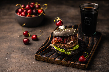 Black Burger with cherry sauce. Cheeseburger with black bun on dark background