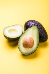 Two Haas avocado fruits on yellow colored  background. Slice avocado