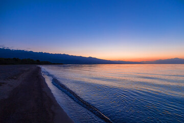 Dawn of the sun at sea. The rising sun behind the mountains. Kyrgyzstan.