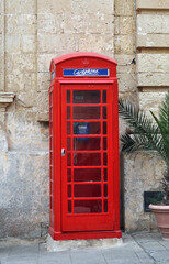 Fototapeta premium Red telephone booth next to the wall of an traditional house in the Old town of M'Dina ,Malta, Europe 