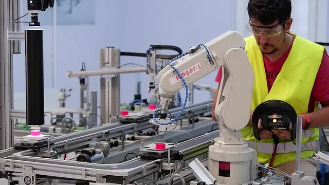 Man with surgical mask and gloves against COVID-19 ( Coronavirus ) programming robot arm with teach pendant. industry 4.0 : smart factory production line control with automation.