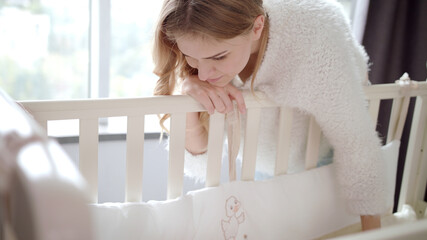 Happy mother near baby crib. Mom looking on sleeping child in cot
