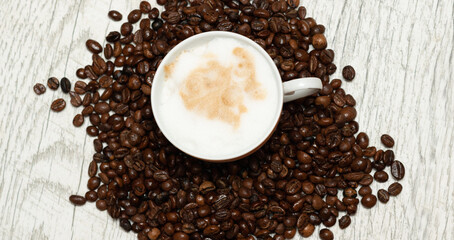 Small cup of cappuccino with coffee beans isolated on light background