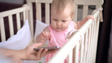 Cute baby in crib touch smartphone. Baby technology concept