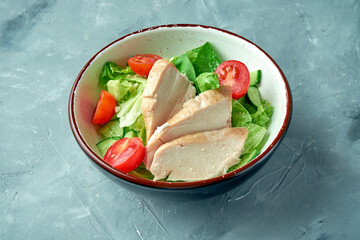 Healthy salad with boiled chicken fillet, lettuce, tomatoes and cucumber in a white bowl on a gray background