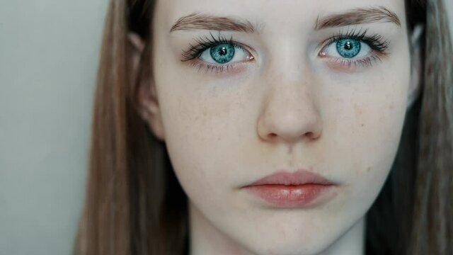 Close-up of young beautiful blue eyes, young teenager girl looks at the camera in slow motion