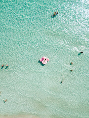 Aerial view of young woman in bikini lie on plastic pink flamingo in azure sea water, swim, sun bathe, people relax on beach Punta Prosciutto, Italian Maldives Puglia Italy. Summer time vacation