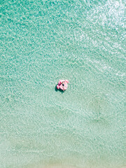 Aerial view of young sexy girl in black swimwear lie on inflatable pink flamingo in azure sea water, swim, sun bathe relax on beach Punta Prosciutto Italian Maldives Puglia Italy. Summer time vacation