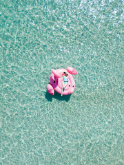 Aerial view young sexy blonde woman in cyan color swimwear lie on inflatable pink flamingo on azure sea, swim, sun bathe relax on beach Punta Prosciutto Italian Maldives Puglia Italy. Summer vacation