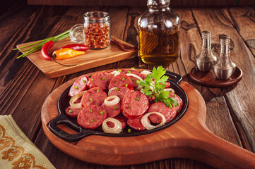 Sliced smoked calabrese sausage with onion in a wooden background - Brazilian appetizer